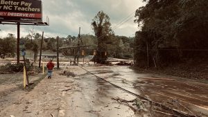 Damage caused by Hurricane Helene. A man walks down a flooded road with downed power lines and debris.