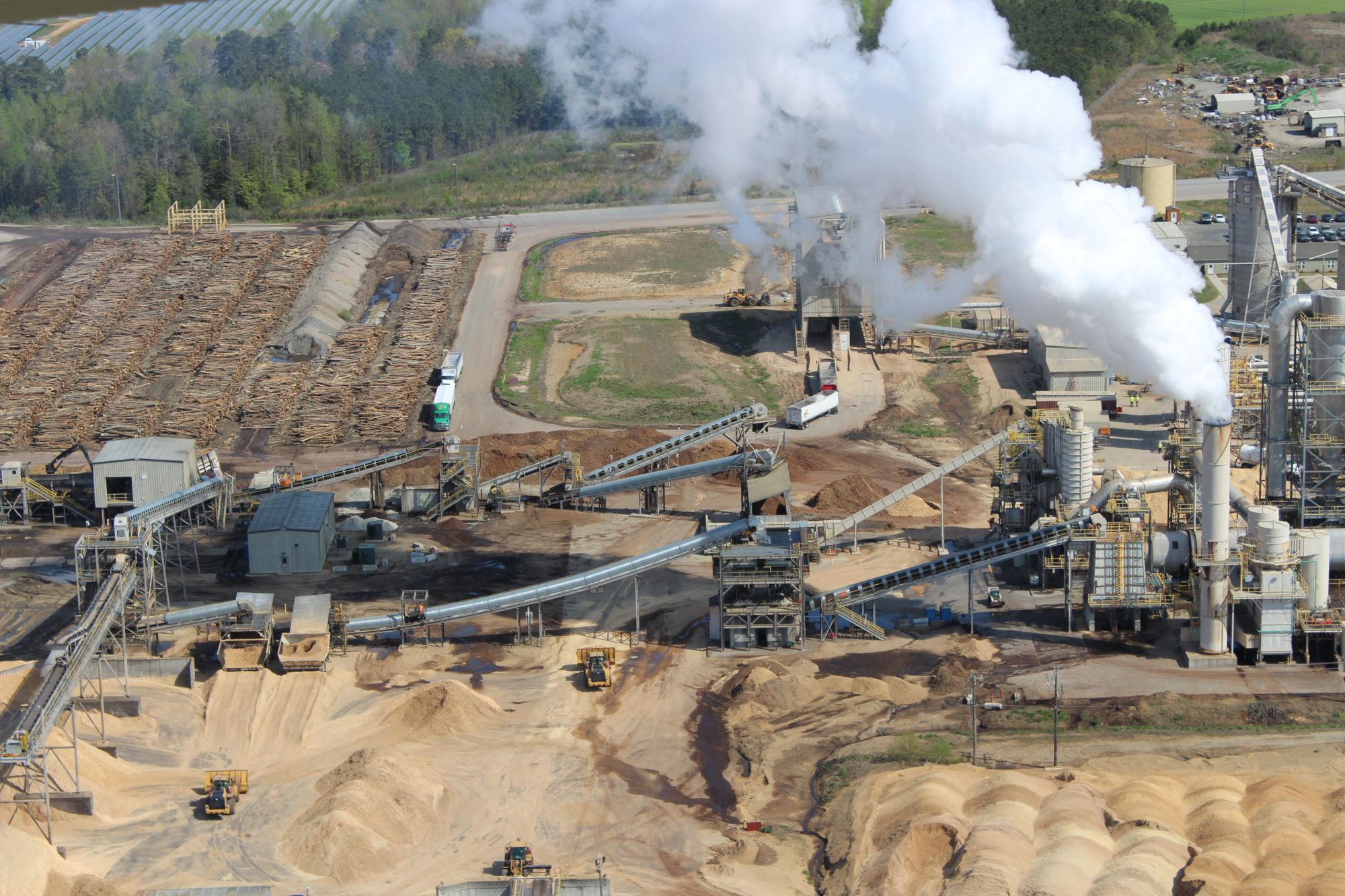 industrial facility with smoke, many cut trees, and mountains of sawdust 